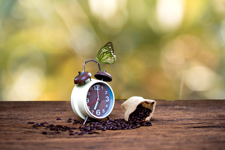 Alarm clock with coffee beans and butterfly on wooden table with morning light, Start up conceptの写真素材
