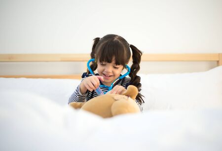Cute kid girl playing doctor with plush toy at homeの写真素材