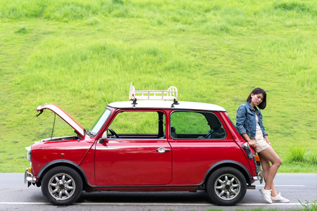 Young woman using mobile phone while looking at broken down car on streetの写真素材