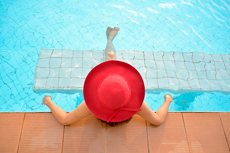 Young woman in red big hat relaxing on the swimming pool, near the sea in the sunsetの写真素材