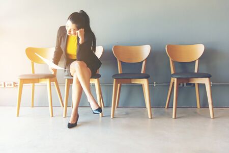 Tired of waiting. Businesswoman holding paper and looking away while sitting on chair against grey backgroundの写真素材