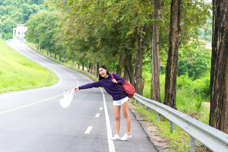 Happy pretty young woman with hand up calling passing car on countryside street,の写真素材