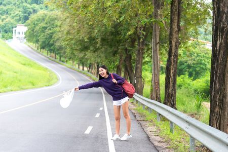 Happy pretty young woman with hand up calling passing car on countryside street,の写真素材