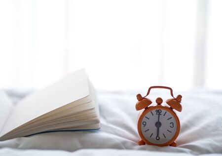 Alarm clock and book on bed in morning with sun lightの写真素材