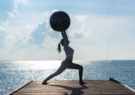 Yoga ball, pilates ball young woman in the beach sunrise backgroundの写真素材