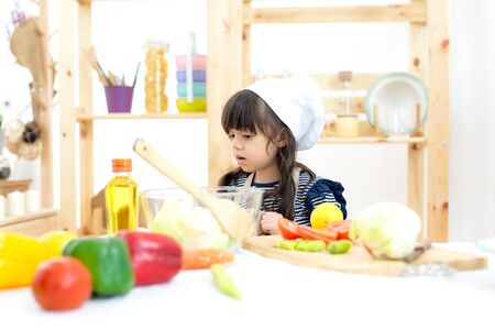 Beautiful kid girl cooking and cutting vegetables on kitchenの写真素材