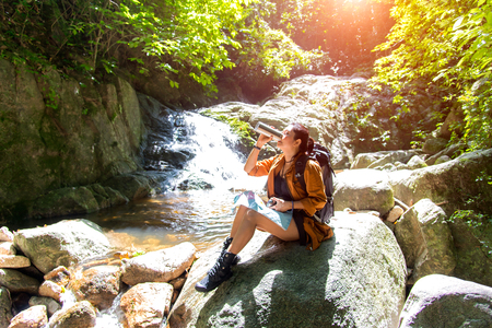 Hiker asian woman drinking water after look binoculars in the water fall, background forest.  Concept Travelの写真素材