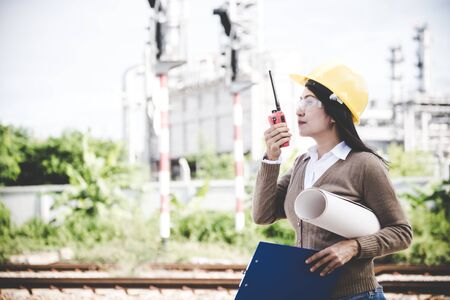 Engineers woman holding radio, blueprint and report schedule for workers security control at power plant energy industry. Engineer Conceptの写真素材