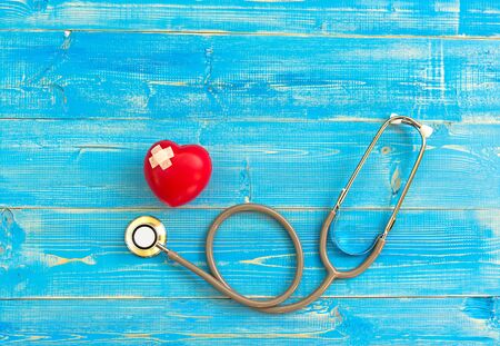 One single alone red heart love shape hand exercise ball with bandage MD medical doctor physician's stethoscope blue wood background.  Healthy Concept.の写真素材