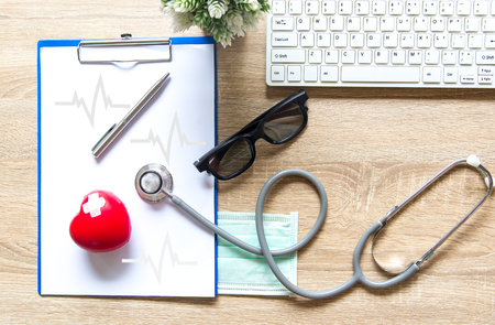 The doctor with a medical stethoscope check heart near a laptop on a wooden tableの写真素材
