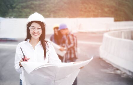 Engineers asia woman holding blueprint with radio for workers security control at power plant energy industry. Engineer Conceptの写真素材