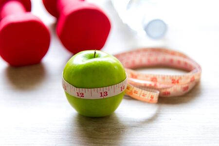 Healthy lifestyle for women diet with sport equipment, sneakers, measuring tape, fruit healthy green apples and bottle of water on wooden, select focus.  Healthy Concept.の写真素材