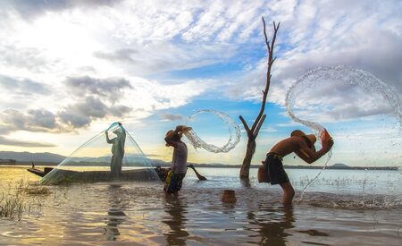 Asian boy and girl playing in the river with fisherman, in the morning sunrise, Thailandの写真素材