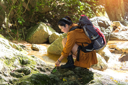 Women hiker with backpack checks map to find directions in wilderness area at waterfalls and forest. Travel Conceptの写真素材