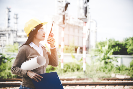 Engineers woman holding radio, blueprint and report schedule for workers security control at power plant energy industry. Engineer Conceptの写真素材