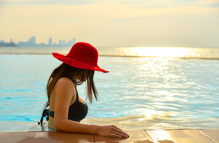 Happy smiling asian woman with straw hat relax and luxury in swimming pool, background sunset.  Summer Conceptの写真素材