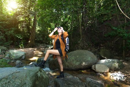 Women hiker with backpack checks map to find directions and look binoculars in wilderness area at waterfalls and forest. Travel Conceptの写真素材