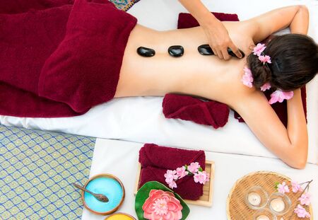 Asia beauty woman lying down on massage bed with traditional hot stones along the spine at Thai spa and wellness center, so relax and lifestyle.  Healthy Conceptの写真素材