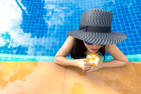 Lifestyle Woman in swimsuit relaxing and happy with cocktail on chaise-longue near swimming pool, summer day.  Summer Concept.の写真素材