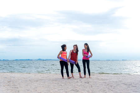Smiling women yoga outdoor on the beach. Young athletic women friends with yoga mats background seashore.  Healthy Conceptの写真素材