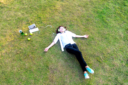 Young women lying in summer grass with headphones listening to music and playing notebook relaxing, sunny day, greenery tone 2017の写真素材