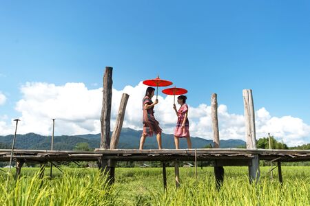 The Women holding a red umbrella and walk on the wooden bridge in the green rice field. Mae Hongson Thailand.  Travel Conceptの写真素材