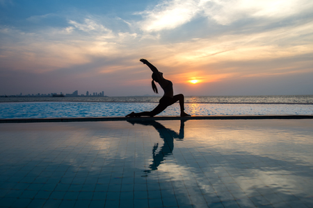 Silhouette young woman practicing yoga on swimming pool and the beach at sunset.  Healthy Concept.の写真素材