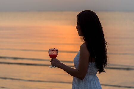 Beautiful woman enjoy and relax with holding cocktail at sunset beachの写真素材