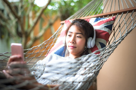 Young woman listening music with smart phone relax lying in a hammock in the holiday.  Lifestyle Concept.の写真素材