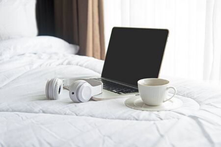 The laptop working on the white bed and coffee in the sunny day morning holiday.  Lifestyle Concept. soft and select focusの写真素材
