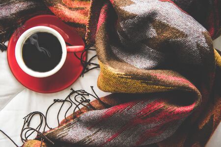 Cozy winter home background, cup of hot coffee with marshmallow, warm knitted sweater on white bed...