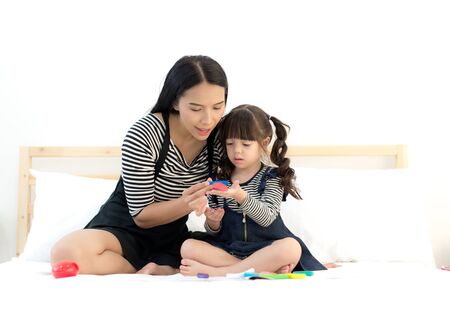 Asian Young mother and little daughter playing with colorful toy clay on the white bed. Lifestyle Conceptの写真素材