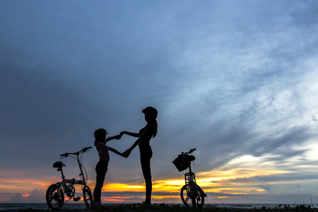 Silhouette biker lovely family at sunset over the ocean.  Mom and daughter bicycling at the beach.  Lifestyle Concept.の写真素材