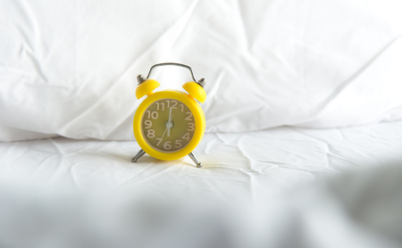 Yellow Alarm clock on bed in morning with sun lightの写真素材