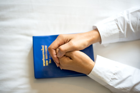 Close up hand woman praying, hands clasped together on her Bible in the bed.の写真素材