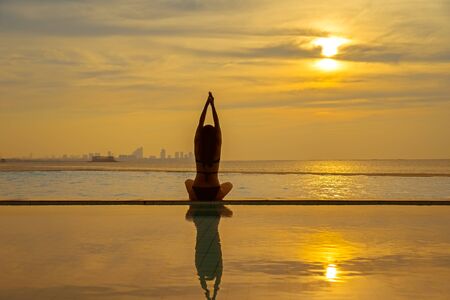 Silhouette young woman practicing yoga on swimming pool and the beach at sunset.  Healthy Concept.の写真素材