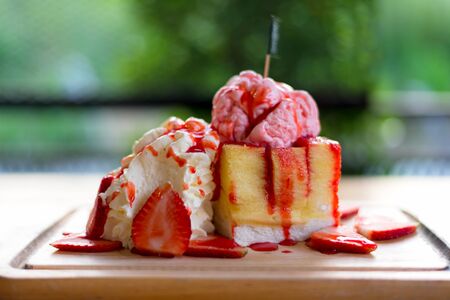 Summer ice fresh.  Toast bread with strawberry ice cream topping, strawberry fruit and jam syrup, green nature background.の写真素材