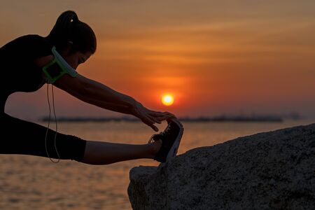 Healthy asian woman athlete stretching legs for warming up before running in the park on sunset.  Health and Lifestyle Conceptの写真素材
