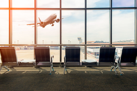 Airport terminal interior with empty seats, background a flying by airplane.の写真素材