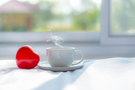 Fresh Cozy morning coffee on the white bed with red heart shape near window in the sunny day, green nature background.  Lifestyle & Valentine Conceptの写真素材