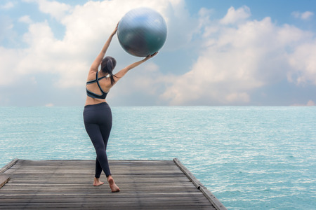 Healthy woman lifestyle balanced yoga ball practicing meditate and energy on the bridge in morning the seashore. Healthy Concept.の写真素材