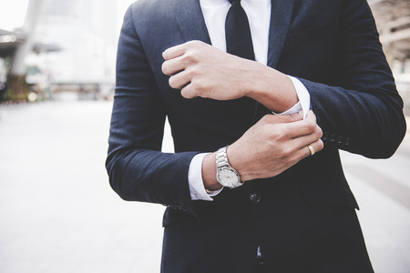 Businessman in full suit adjusting his sleeve and looking away while standing relax outdoors with model cityscape in the background.  Business Lifestyle Conceptの写真素材