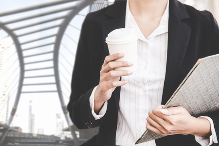 Close up of businesswoman holding a coffee cup and document report walking in the cityscape haste time.   Business and Lifestyle Conceptの写真素材