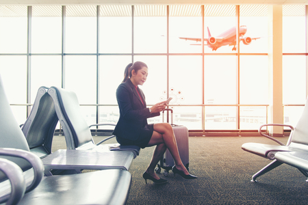 Business asian women passenger using mobile payments banking online shopping and icon e customer network connection on screen commerce, multichannel and channel for worldwide.  Women waiting at the airport for plane departure with luggage.  Lifestyle Concept.の写真素材