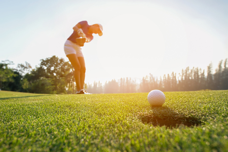 Golfer asian woman focus putting golf ball on the green golf on sun set evening time.. Healthy and Lifestyle Conceptの写真素材