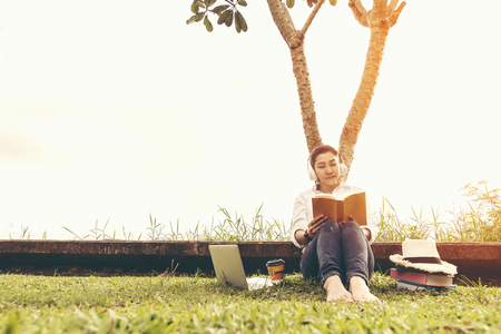 Lifestyle women enjoy listening music and reading a book and play laptop on the grass field of the nature park, vintage tone.  Lifestyle Concept.の写真素材