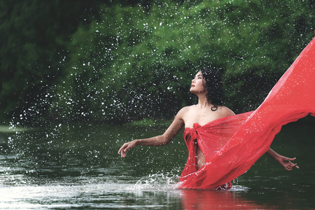 Asian woman relaxing and enjoying playing with water and splash at tropical exotic river with turquoise amazing color water in beautiful destination forest. Travel Conceptの写真素材