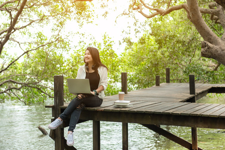Asian women working and  drinking coffee after education nature and forest input the laptop under big tree.  The mangrove forest nurture environmental and reduce global warming earth.  Ecology Conceptの写真素材