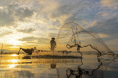 Fisherman action when fishing net  on lake in the sunshine morning and silhouette fisherman on the boat,  Thailandの写真素材
