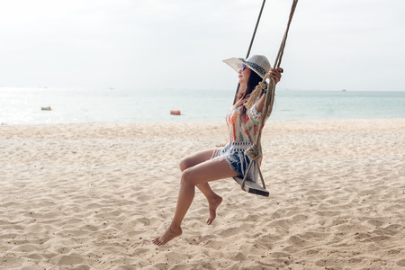 Summer Vacations. Lifestyle women relaxing and enjoying swing on the sand beach, fashion stunning women with white dress on the tropical island so happy and luxury in holiday summer. Travel and Summer Conceptの写真素材